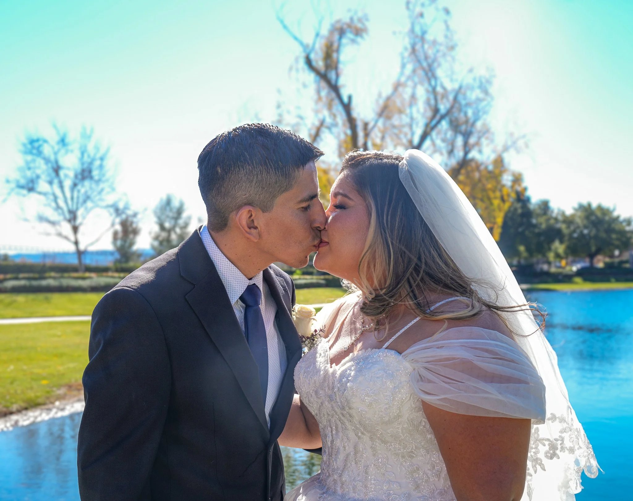 Bride and groom kiss by a lake