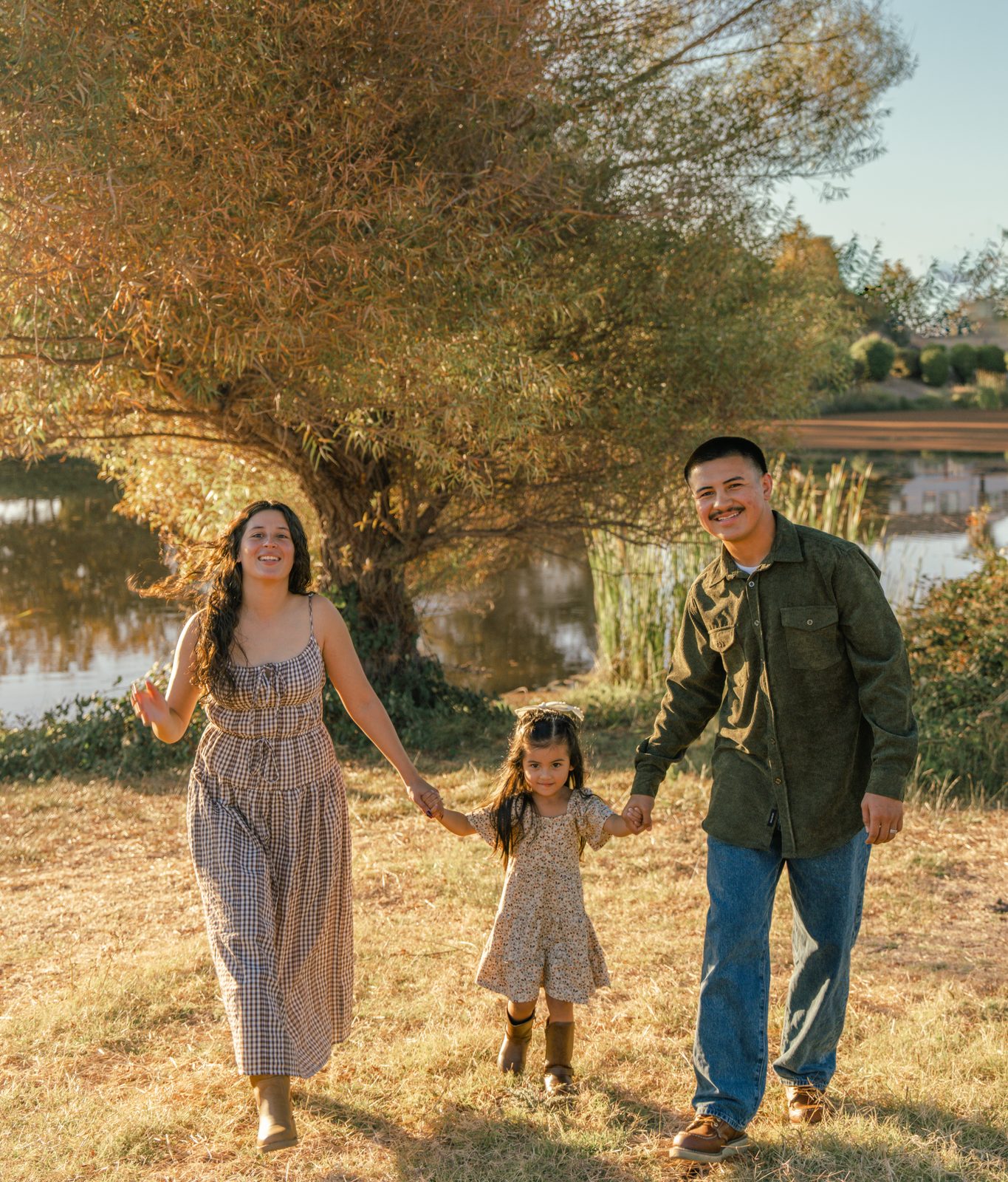 A mother, father and daughter walk hand in hand through golden grass, laughing