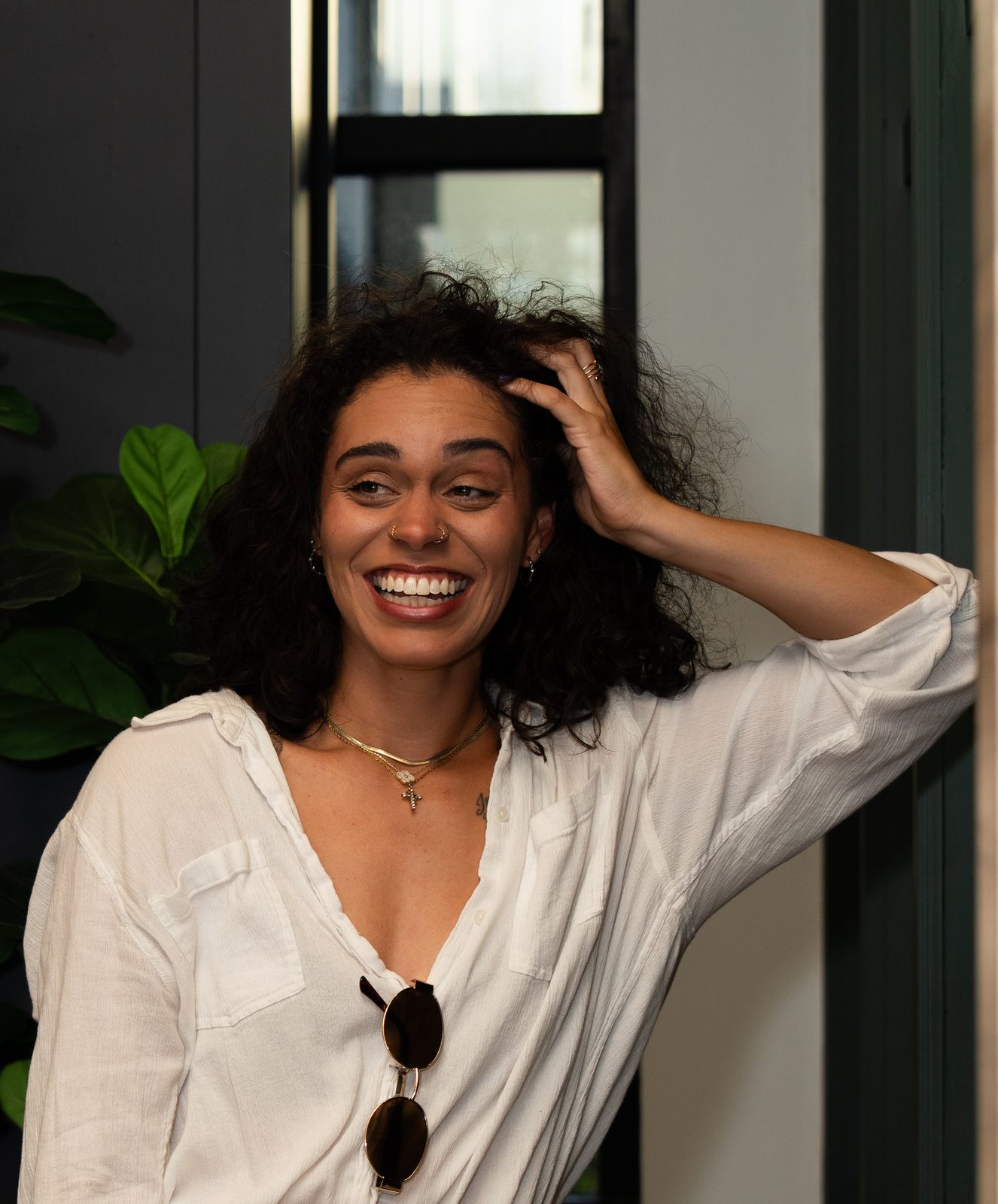 A woman in a white shirt laughing, one hand pushed back into her curly hair