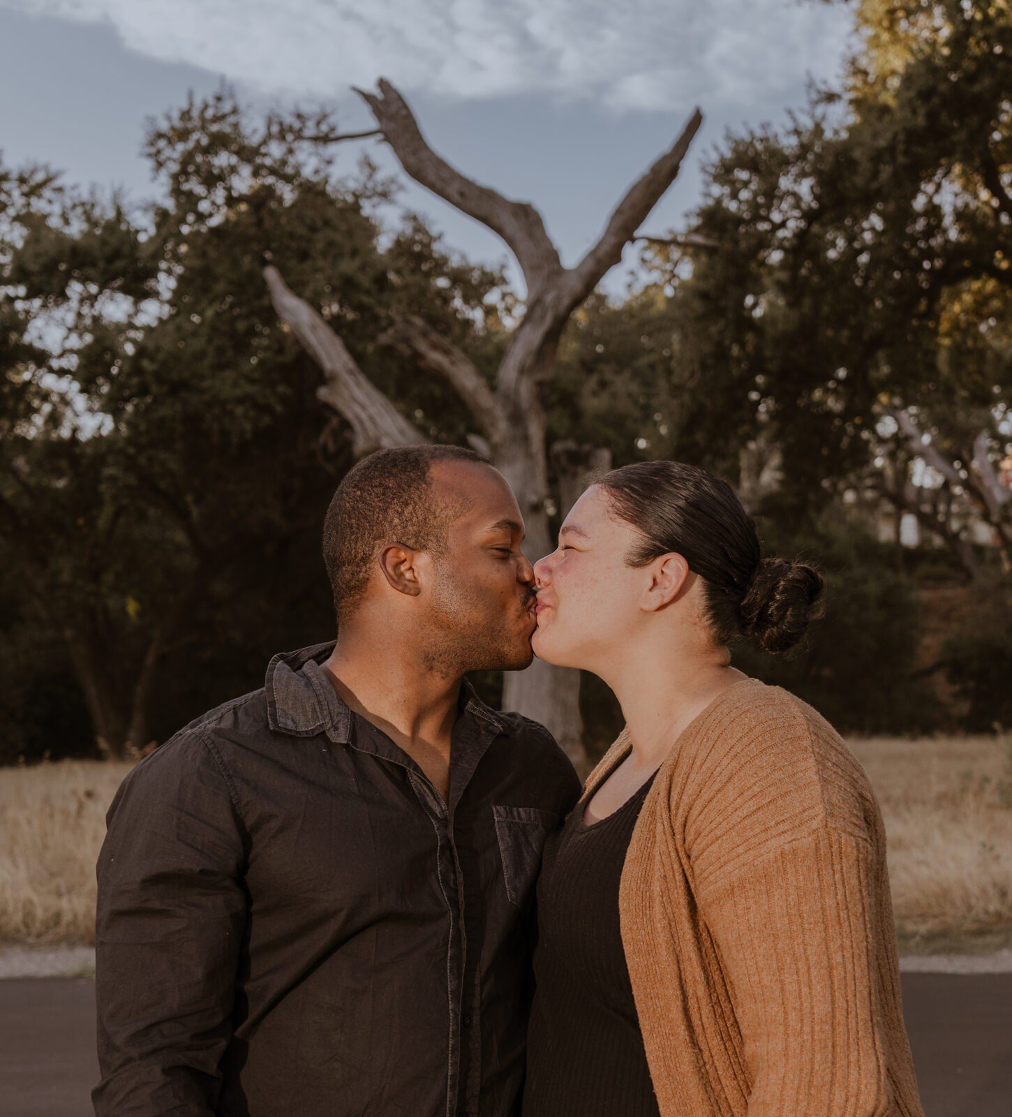Parents sharing a quiet kiss beneath a bare oak